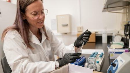 A scientist uses a syringe to put liquid in a test tube.